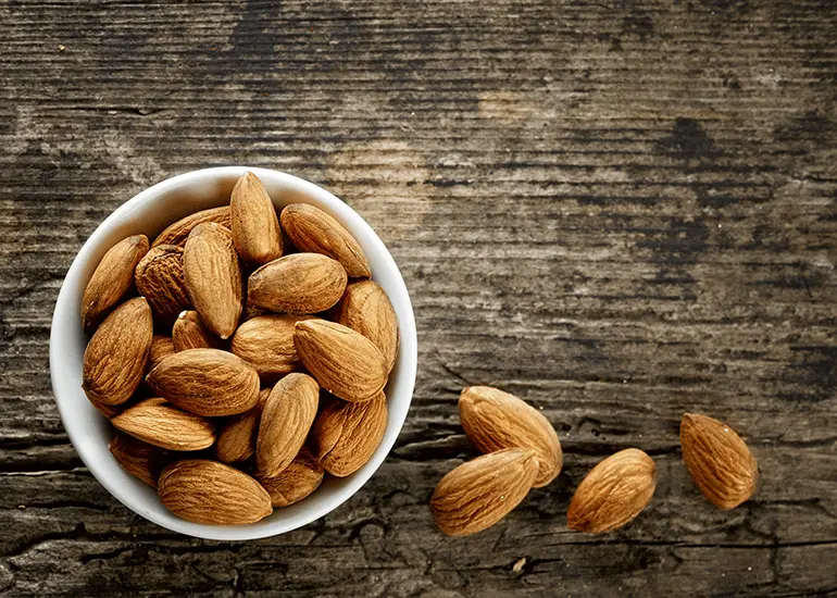 A ramekin of raw almonds on a wooden table