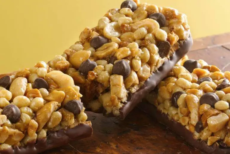 Three nut and chocolate chip granola bars with a chocolate coating, placed on a wooden surface.
