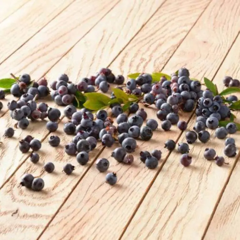 A scattered pile of blueberries with green leaves on a wooden surface.